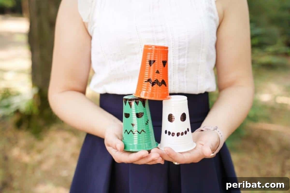A person holding a selection of finished plastic cup Halloween lanterns, showcasing the variety of characters.