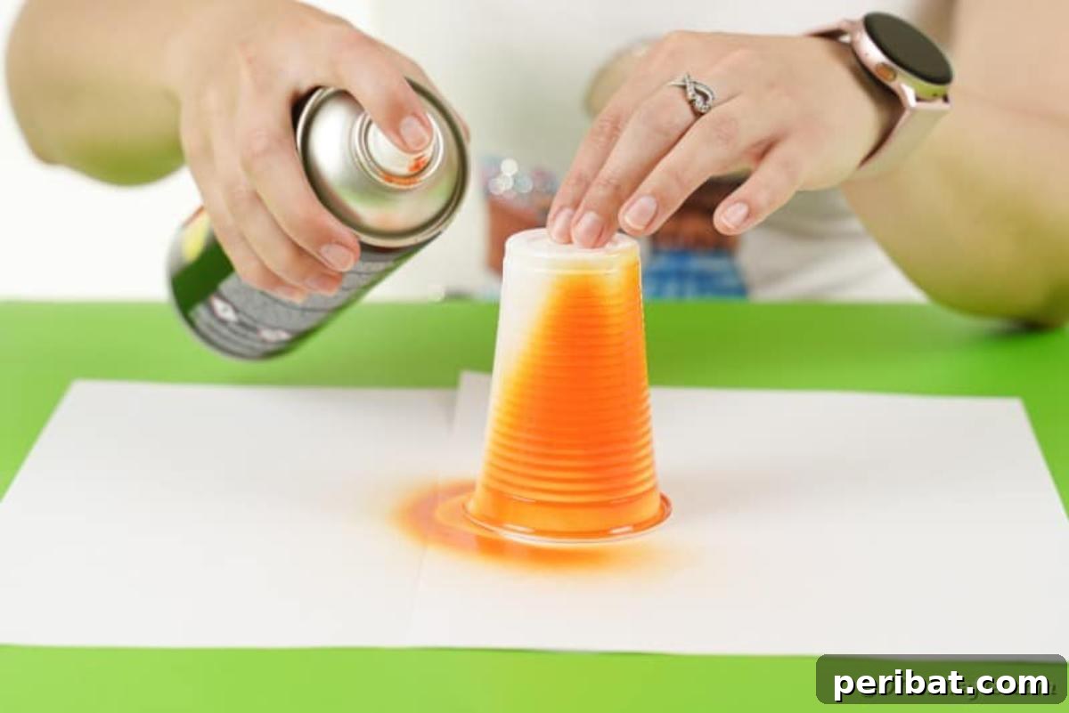 A person spray painting a plastic cup orange, initiating the pumpkin lantern creation.