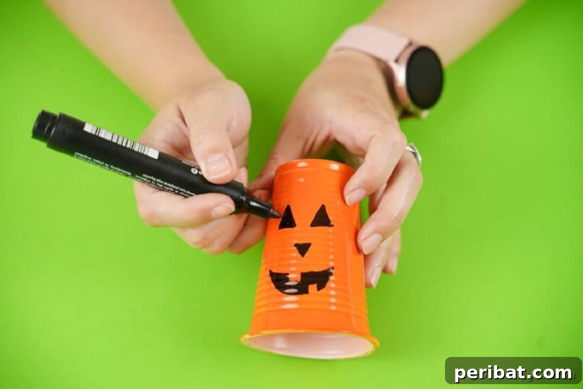 Detail shot of a hand drawing a jack-o-lantern face onto an orange plastic cup.