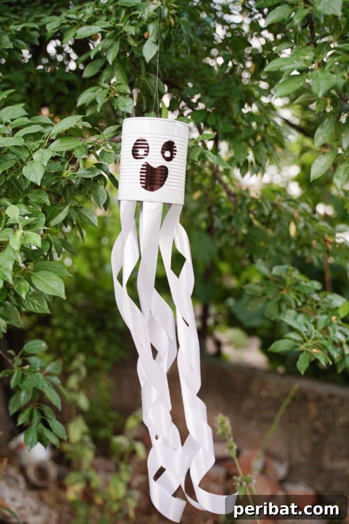 Haunting Tin Can Ghost Ornament 16 A captivating wide shot of a tin can ghost hanging amidst the branches of a tree, blending beautifully with the natural outdoor setting.