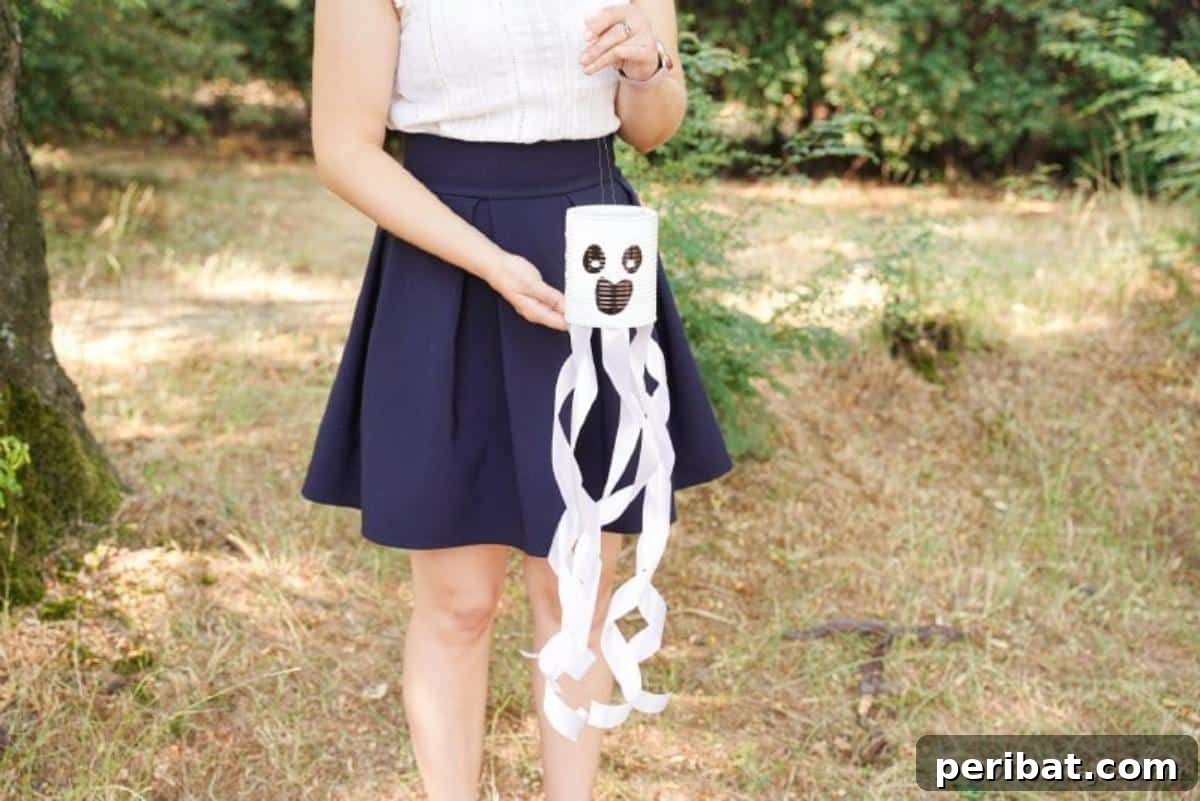 Haunting Tin Can Ghost Ornament 5 A crafter proudly holds a finished tin can ghost decoration, showcasing its simple design and the elegant flow of its white ribbon streamers.
