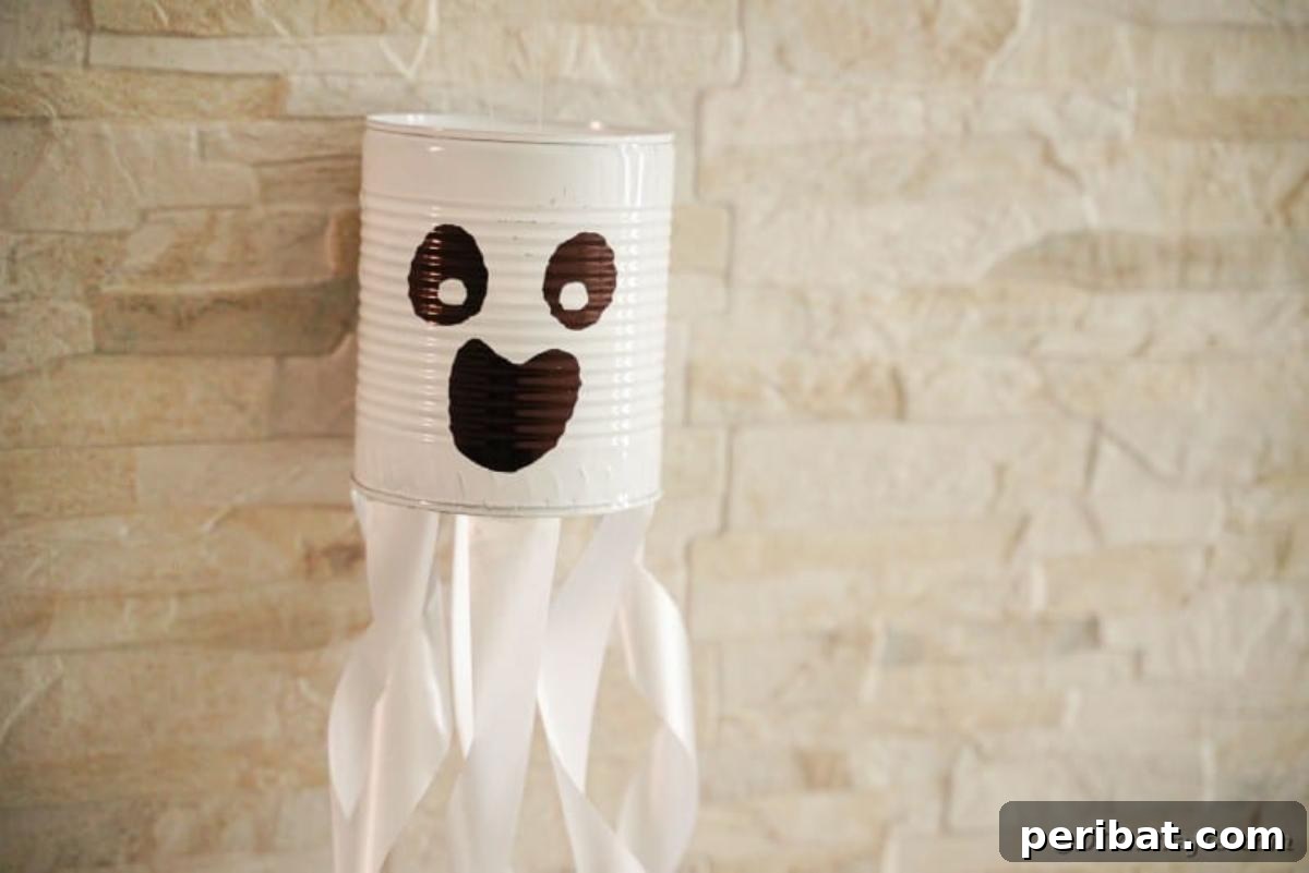 Haunting Tin Can Ghost Ornament 6 A finished tin can ghost decoration displayed against a textured brick wall, showing its painted face and ribbon streamers.