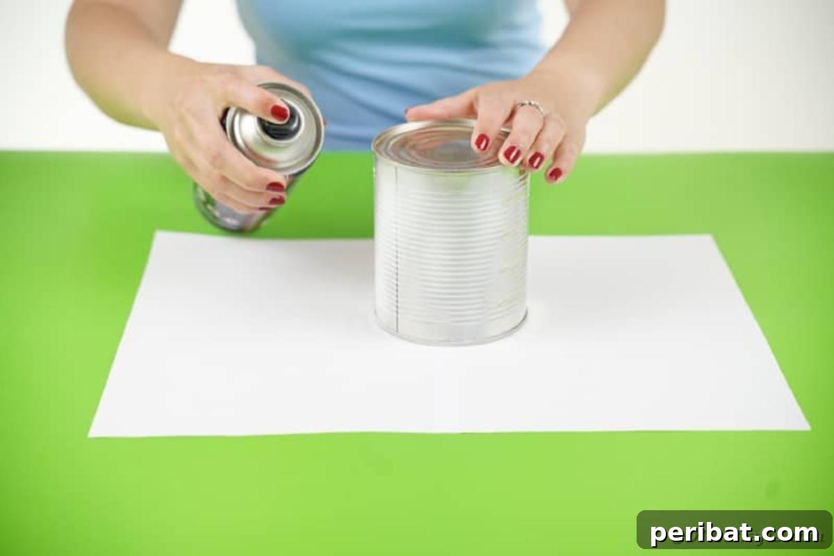 Haunting Tin Can Ghost Ornament 8 A person is shown applying white spray paint to an empty tin can, the first step in creating the ghost decoration.