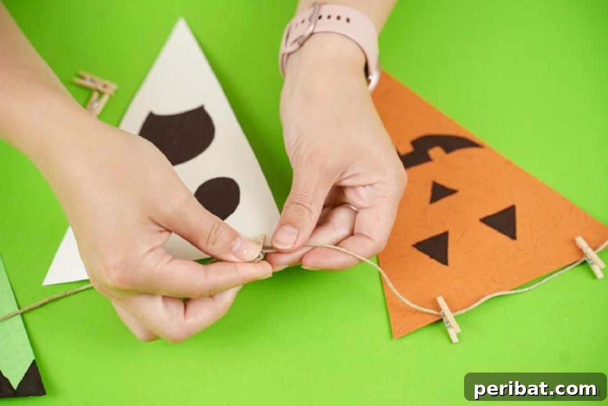 Hands attaching the decorated Halloween character flags to the twine using small clothespins