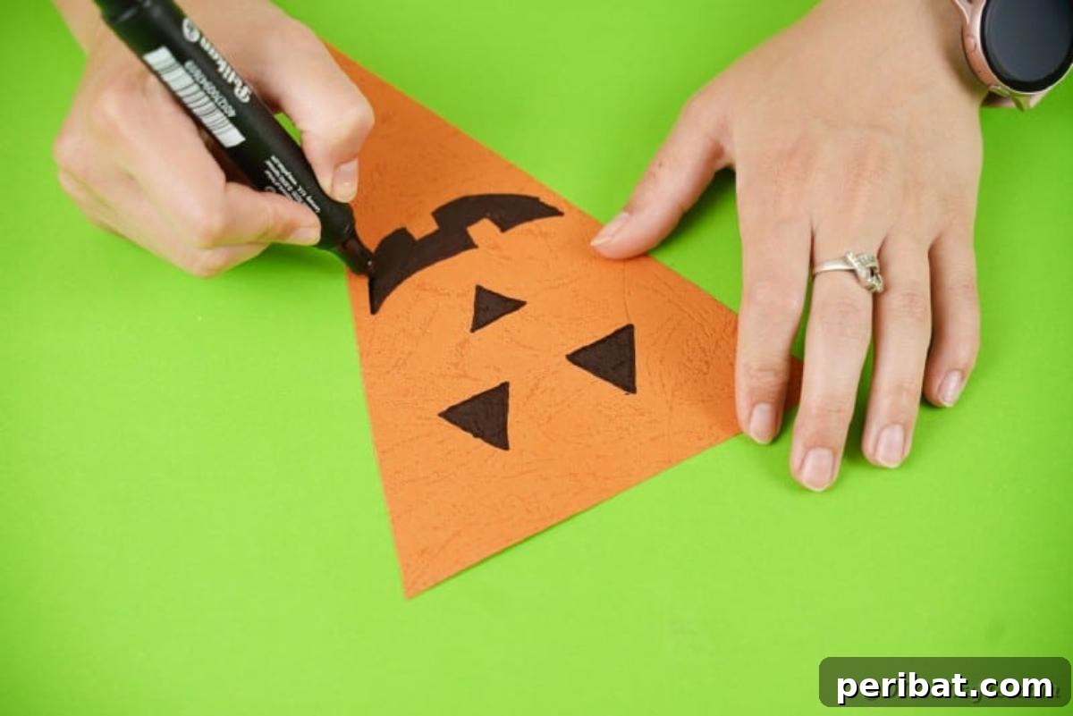 Close-up of an orange paper triangle with a hand-drawn pumpkin face