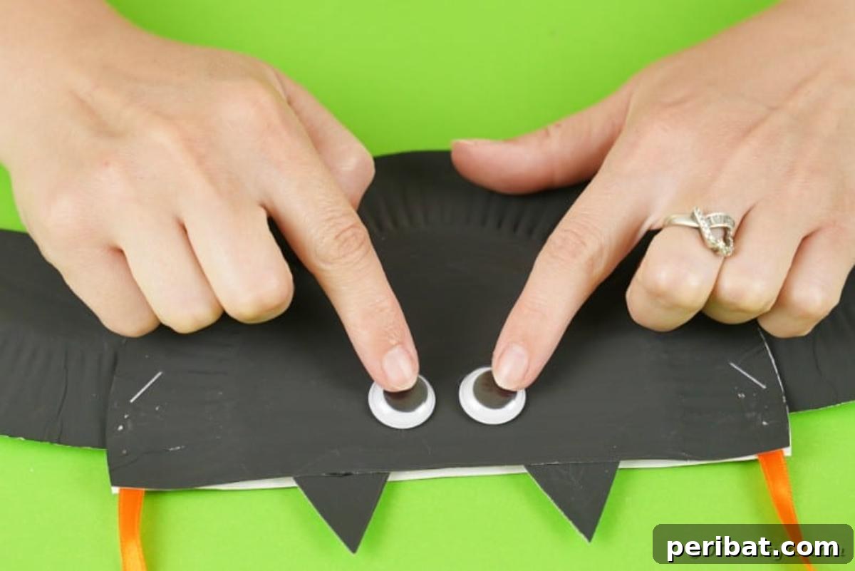 DIY Paper Plate Bat Candy Catchall 19 Gluing googly eyes to front of bat