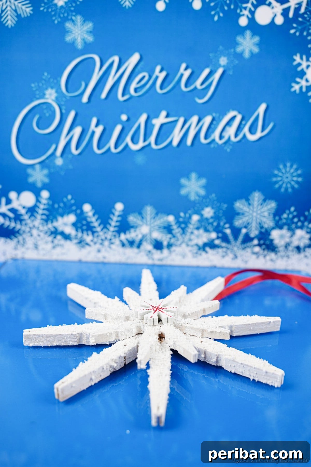 white clothespin snowflake laying on blue table with merry christmas message above