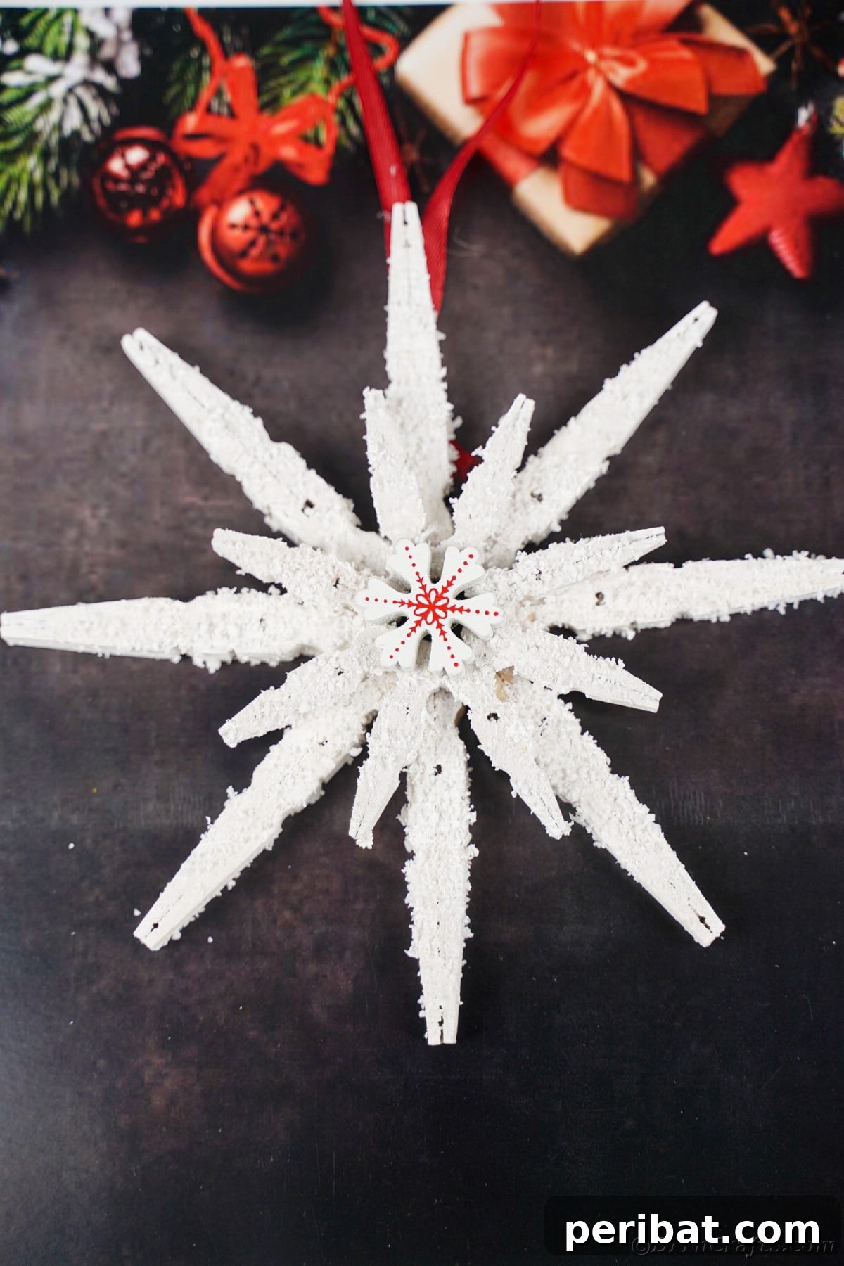 snowflake ornament hanging from red ribbon in front of black background
