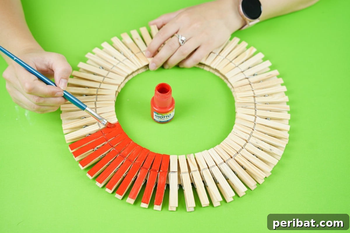Craft a Delightful Santa Hat Wreath for Christmas 15 Painting red craft paint onto wooden clothespins attached to the wreath.