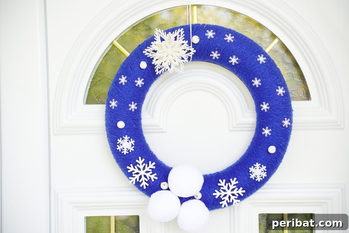 Glistening Snowflake Christmas Wreath 16 Close-up of a beautiful blue winter wreath embellished with snowflakes and pom poms, hanging on a door, ready for the festive season