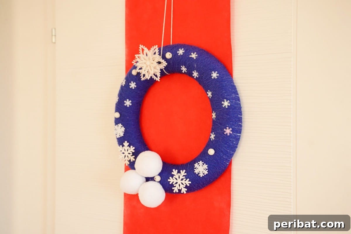 Glistening Snowflake Christmas Wreath 17 Blue and white snowflake wreath hanging over a festive red background on a wall, showcasing its holiday appeal