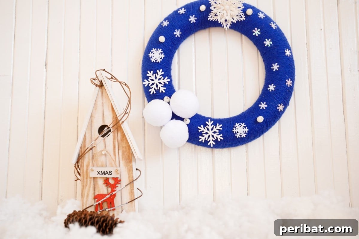 Glistening Snowflake Christmas Wreath 5 Elegant snowflake wreath, featuring blue yarn and white embellishments, displayed next to a charming small wooden house, evoking a cozy winter scene