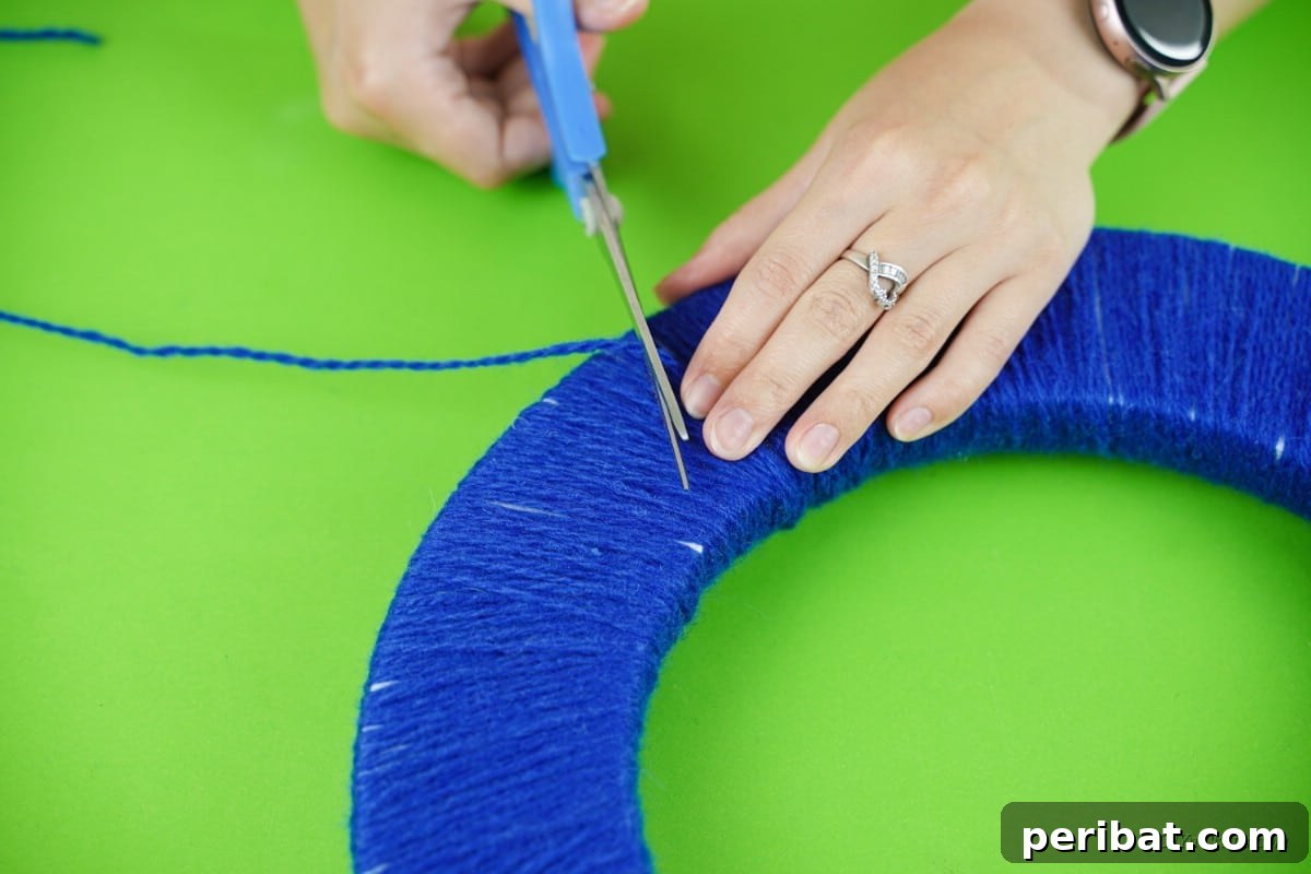 Glistening Snowflake Christmas Wreath 10 Scissors cutting the blue yarn after wrapping, signifying the completion of the wreath's base layer