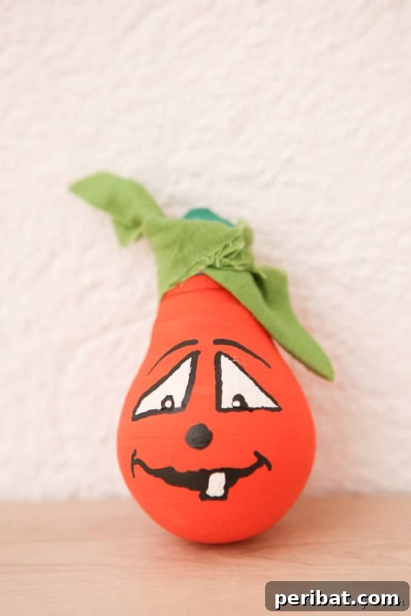 55+ Creative DIY Pumpkin Decorating Ideas for Fall 13 An adorable painted lightbulb pumpkin with a smiling face, resting on a wooden table