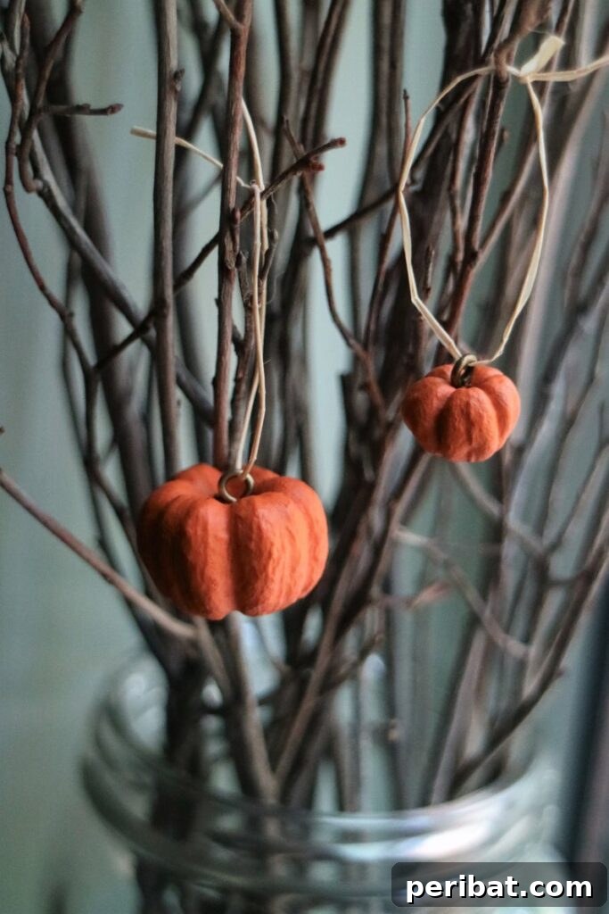 55+ Creative DIY Pumpkin Decorating Ideas for Fall 33 A charming miniature pumpkin ornament hanging from bare branches, perfect for a Fall tree