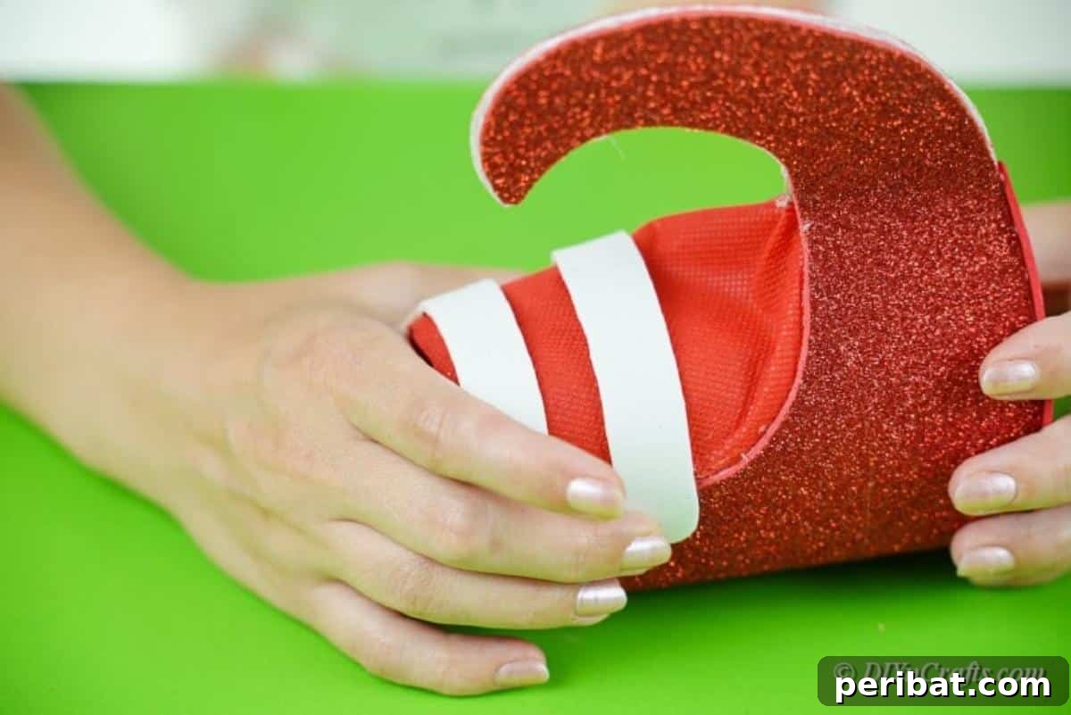Upcycled Plastic Bottle Santa Boot Decor 14 Applying white paper strips as decorative bootstraps onto the red foam craft boot