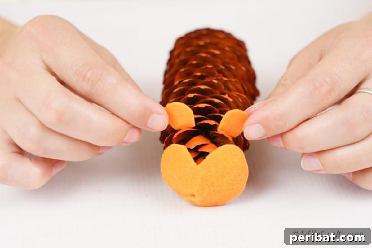 Whimsical Pinecone Hedgehogs 12 A hand gluing a felt face onto a painted pinecone, demonstrating the assembly process of the hedgehog craft.