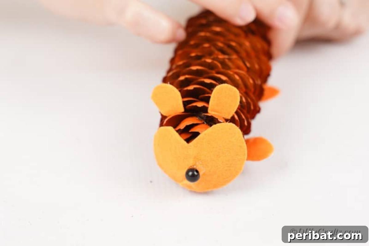 Whimsical Pinecone Hedgehogs 13 A small black bead being glued onto the felt face of a pinecone hedgehog to create its nose, showing a detailed step.
