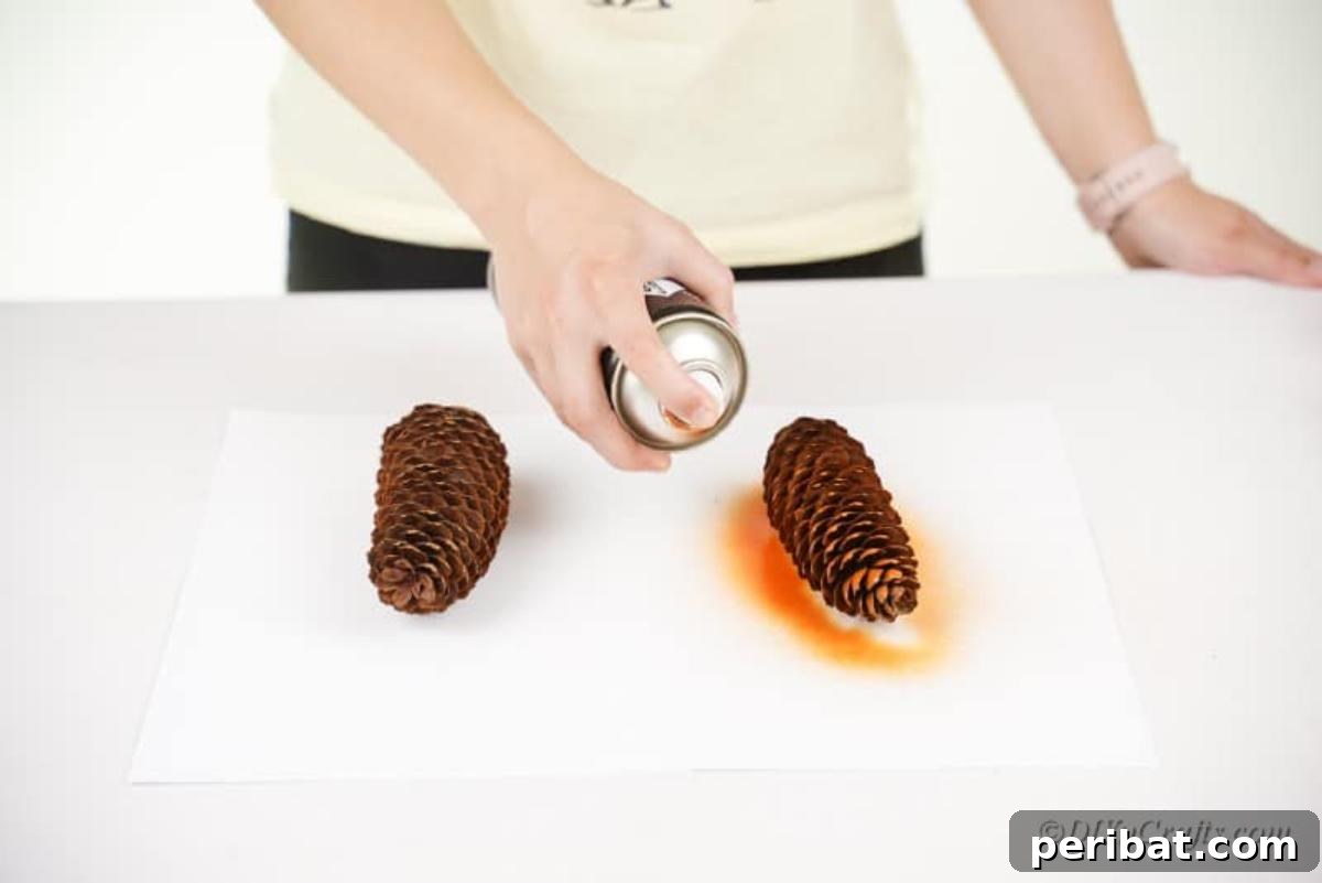 Whimsical Pinecone Hedgehogs 9 A hand spray painting a pinecone orange on a sheet of newspaper, illustrating the first step of the craft project.