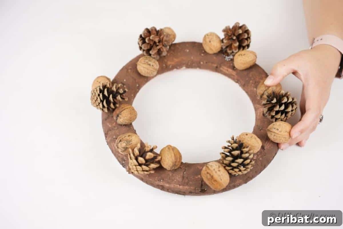 Foraged Fall Wreath 7 placing nuts on a spray painted wreath on the table