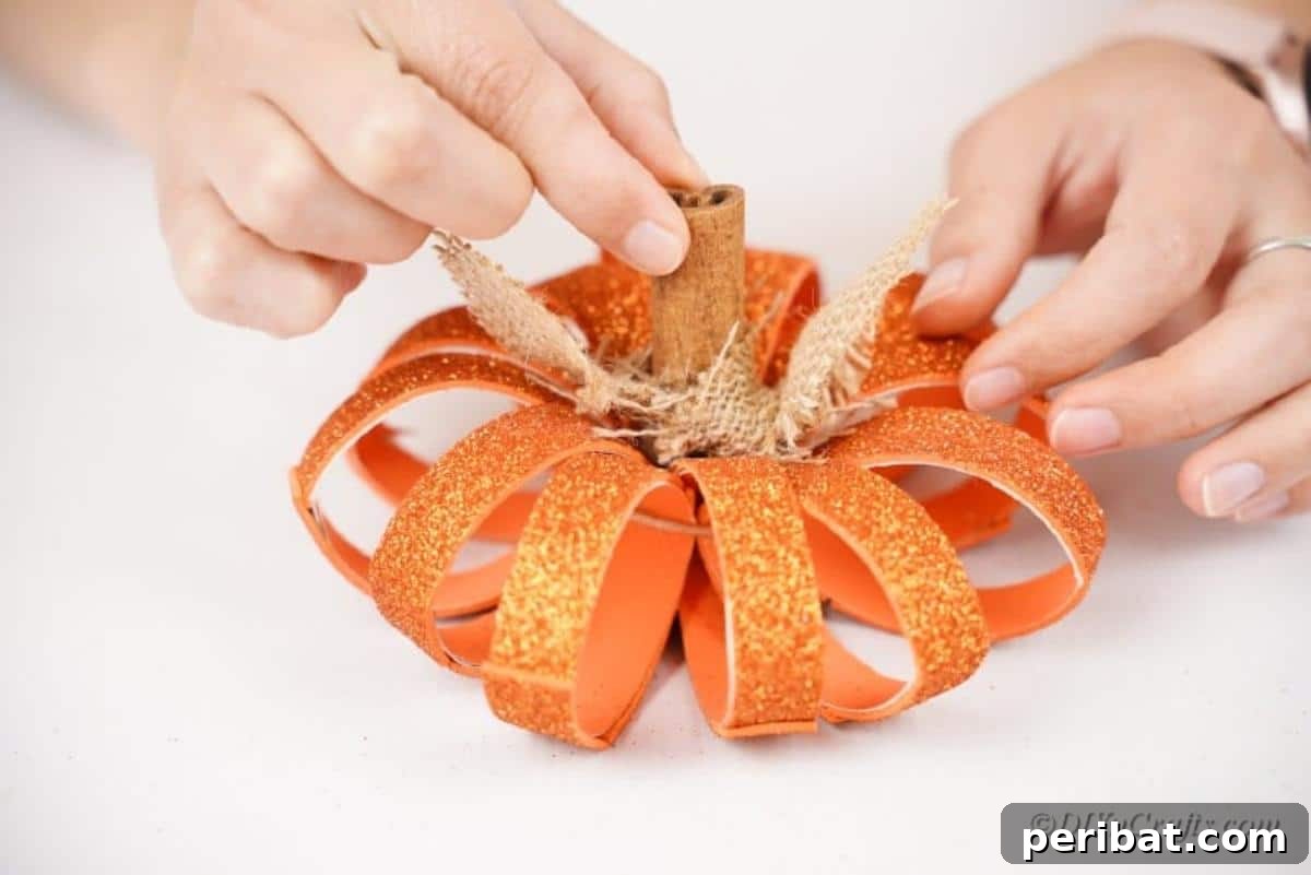 The final decoration step for a toilet paper roll pumpkin craft, showing hands adding details.