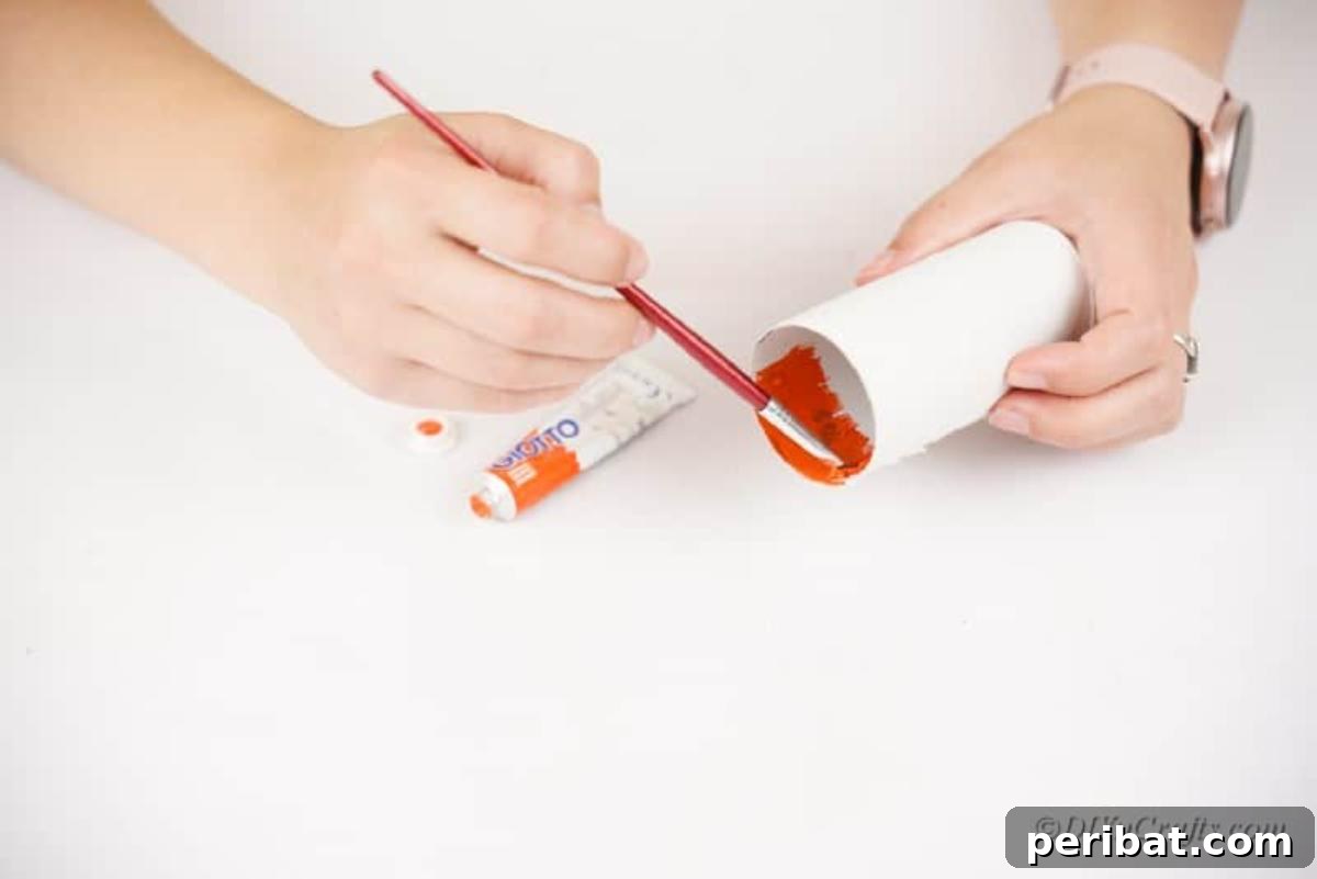 Painting the inside of a toilet paper roll with orange craft paint.