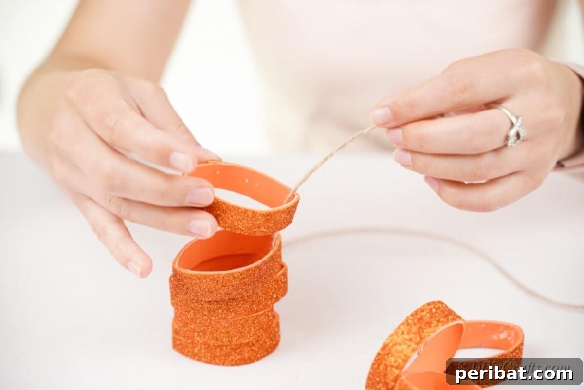 A woman's hands threading twine through stacked toilet paper roll rings to form a pumpkin shape.