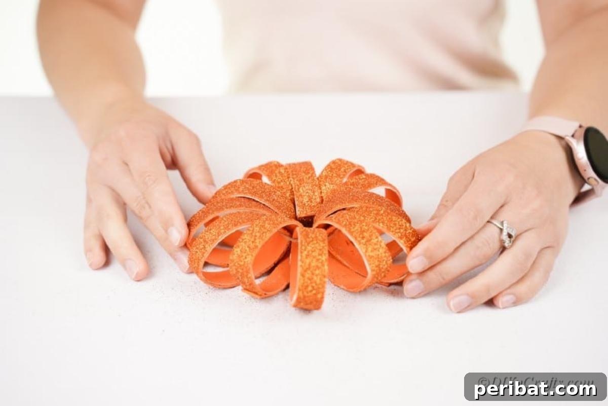Tying off the twine to secure the painted orange toilet paper roll rings into a pumpkin shape.