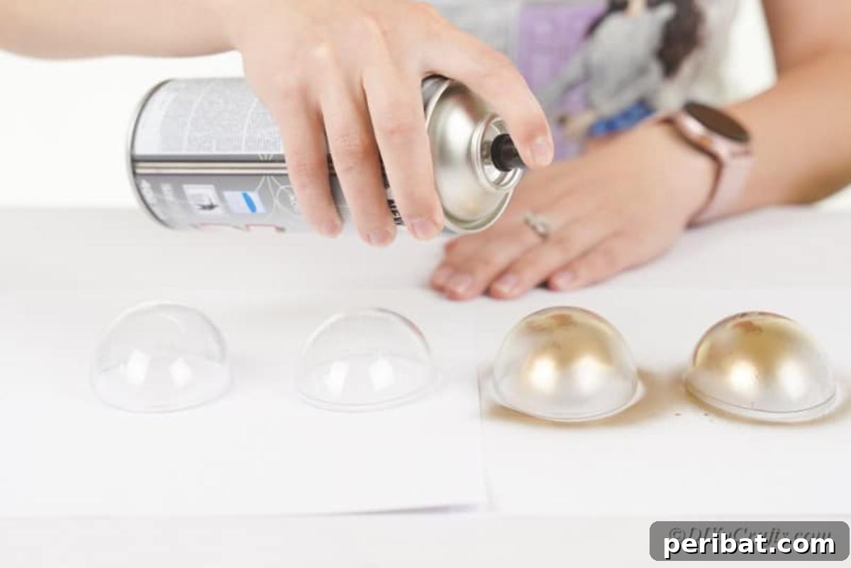 Atık Plastik Yumurtalardan Sonbahar Meşe Palamudu Yapımı 7 A person expertly spray painting a plastic egg half with metallic gold paint for the acorn craft.