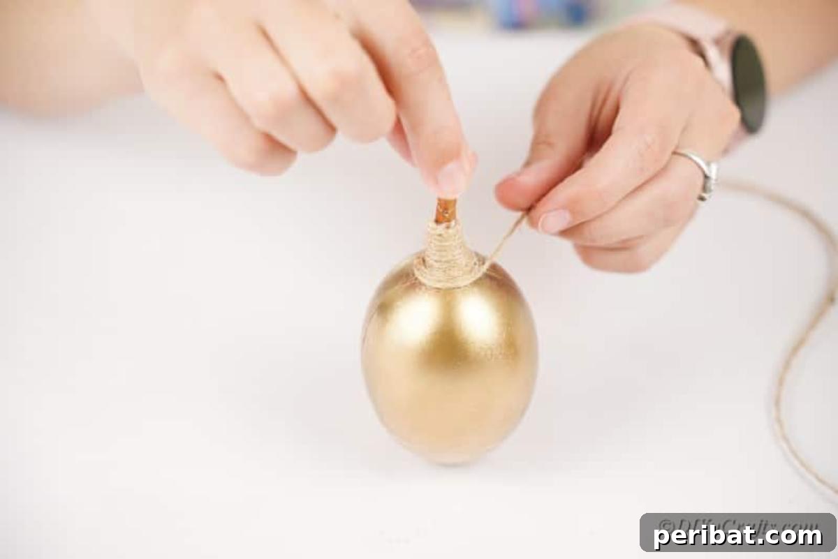 Atık Plastik Yumurtalardan Sonbahar Meşe Palamudu Yapımı 10 A crafter's hands carefully adding twine in a spiral pattern to a golden craft acorn, securing it with glue.