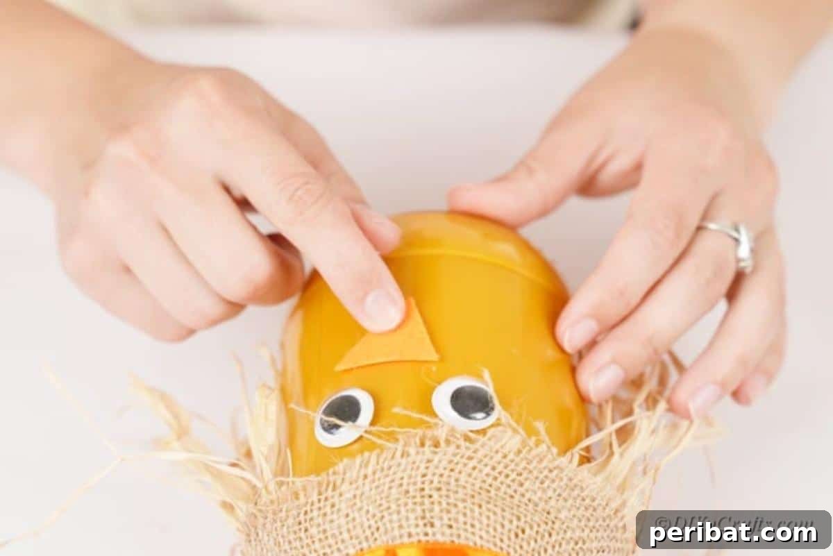 Whimsical Fall Scarecrow Jar Craft 14 A finger gently presses an orange craft foam nose onto the scarecrow jar, completing the central facial feature of the charming autumn craft.