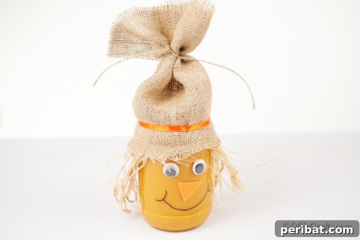 Whimsical Fall Scarecrow Jar Craft 16 The completed scarecrow jar craft, featuring an orange painted body, burlap hat, straw hair, googly eyes, and a hand-drawn smile, ready to display.