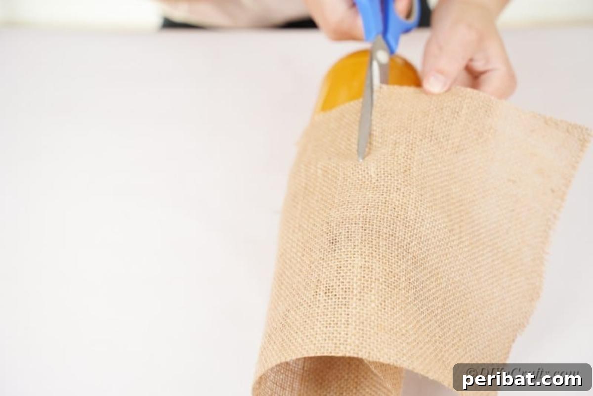Whimsical Fall Scarecrow Jar Craft 8 Scissors neatly cutting a piece of burlap fabric, precisely measured to form the hat for the scarecrow jar craft.