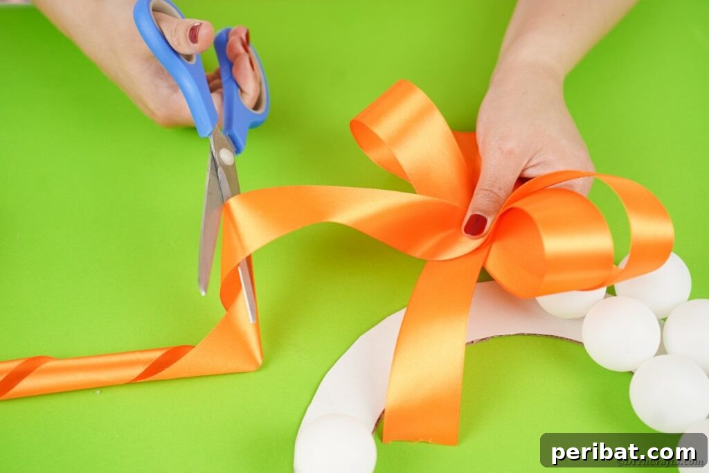 Ghoul's Eye Halloween Entry Wreath 12 A hand holding scissors, poised to cut a vibrant orange ribbon, a preparatory step for tying the wreath's bow