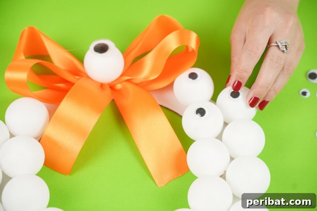 Ghoul's Eye Halloween Entry Wreath 16 Hands carefully gluing googly eyes onto the ping pong balls on the wreath, bringing the monster eyeballs to life