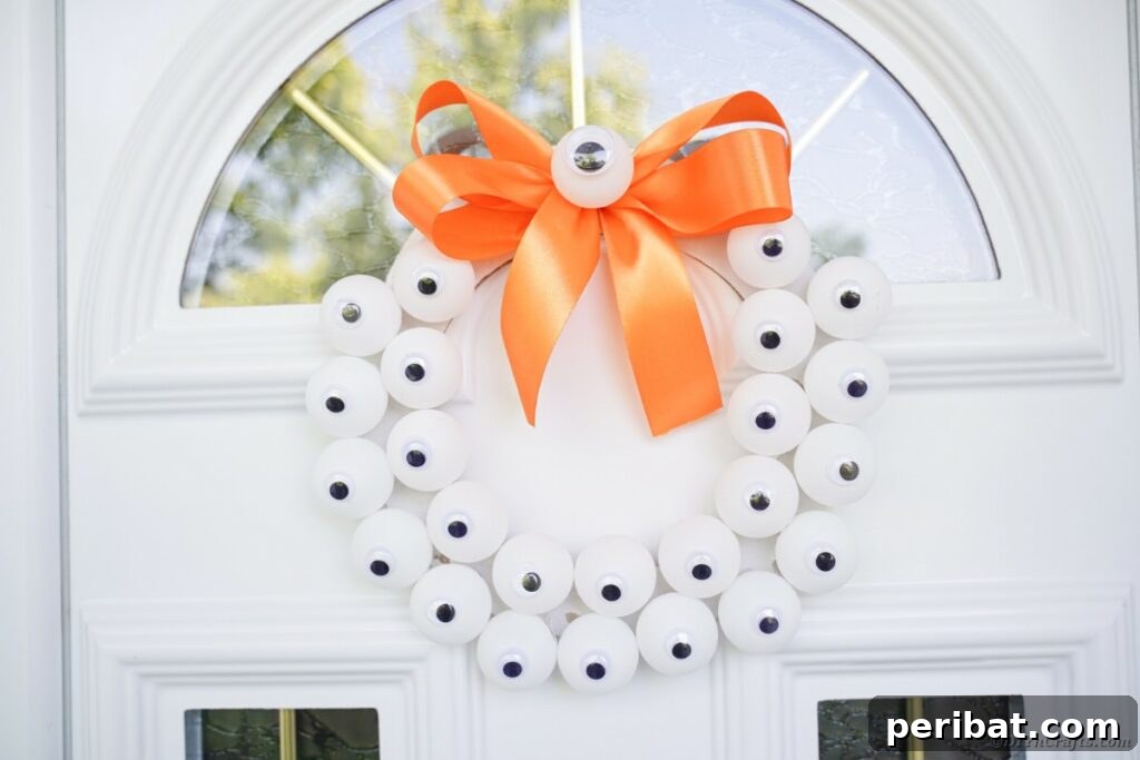 Ghoul's Eye Halloween Entry Wreath 3 A finished monster eyeball wreath elegantly hanging on a pristine white front door, ready for Halloween