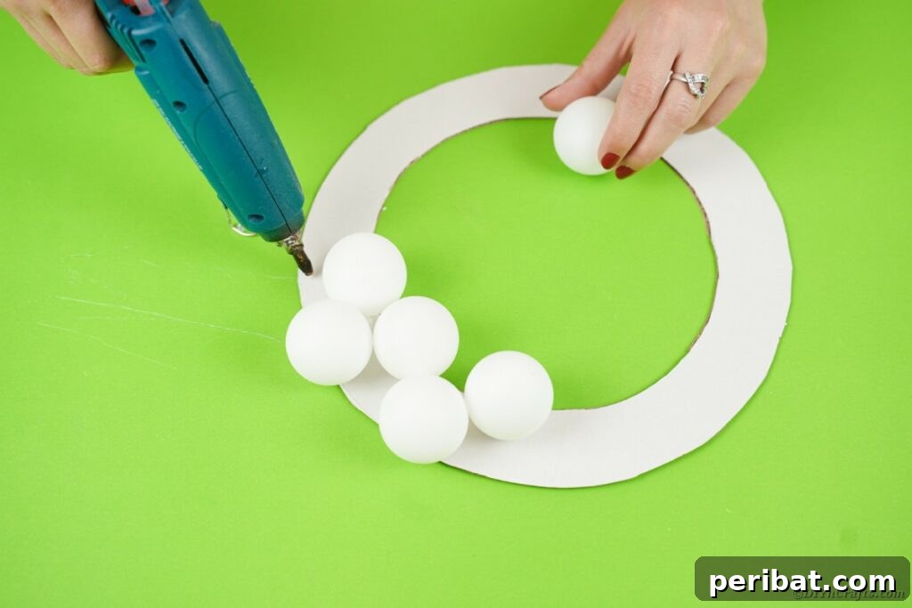Ghoul's Eye Halloween Entry Wreath 10 Close-up view of ping pong balls being carefully glued onto a cardboard wreath base, illustrating the eyeball arrangement