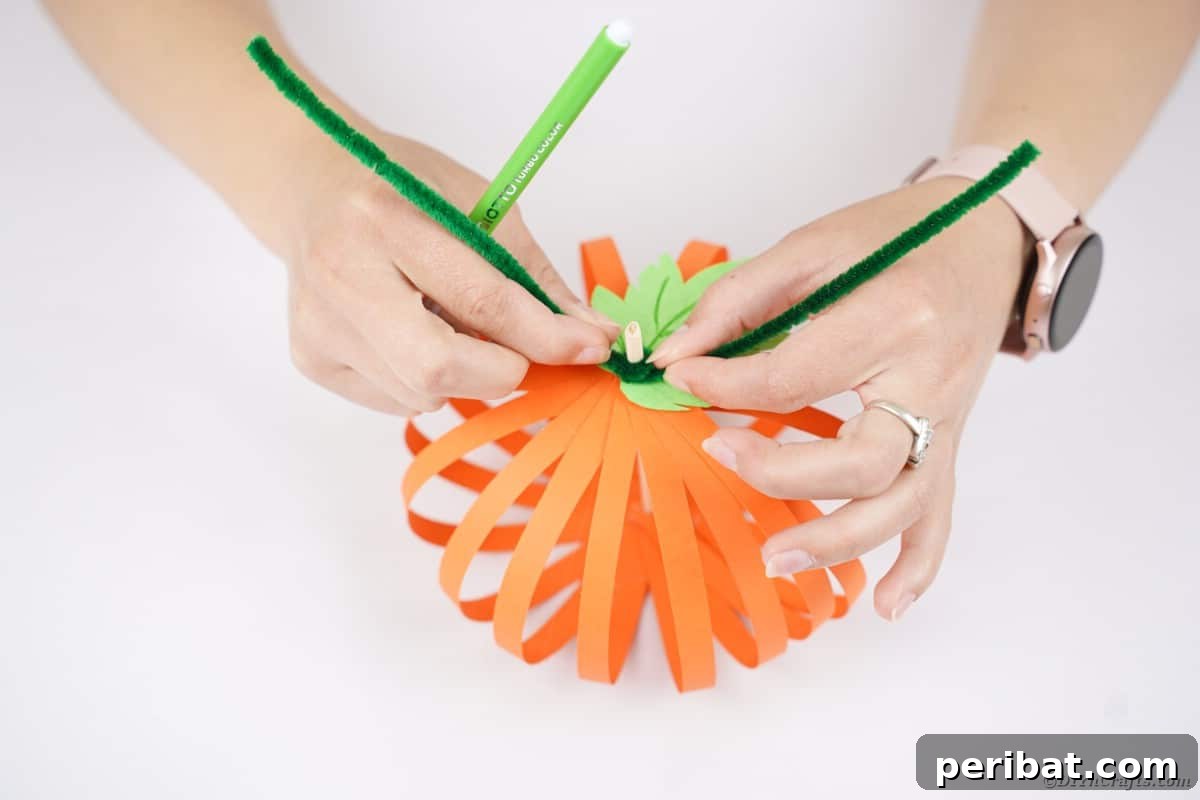 Spooky Paper Strip Creations: Bats, Pumpkins & Spiders 19 A green pipe cleaner being wrapped around the top of the dowel stem, just above the paper leaf, forming tendrils.