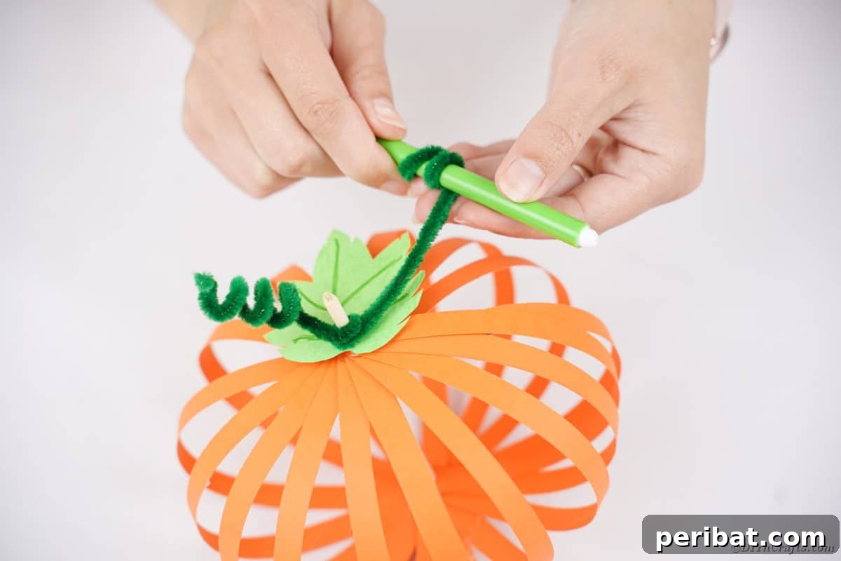 Spooky Paper Strip Creations: Bats, Pumpkins & Spiders 20 A green pipe cleaner being wound tightly around a pen to create a coiled tendril shape.