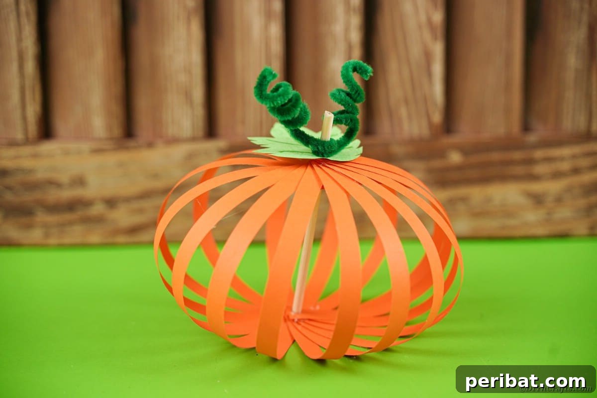 Spooky Paper Strip Creations: Bats, Pumpkins & Spiders 3 A vibrant orange paper pumpkin with a green stem sits on a green table, ready for fall decor.