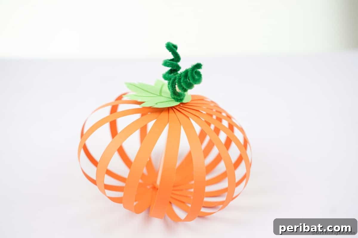 Spooky Paper Strip Creations: Bats, Pumpkins & Spiders 21 A completed orange paper strip pumpkin with a green stem and tendrils, displayed on a wooden table.