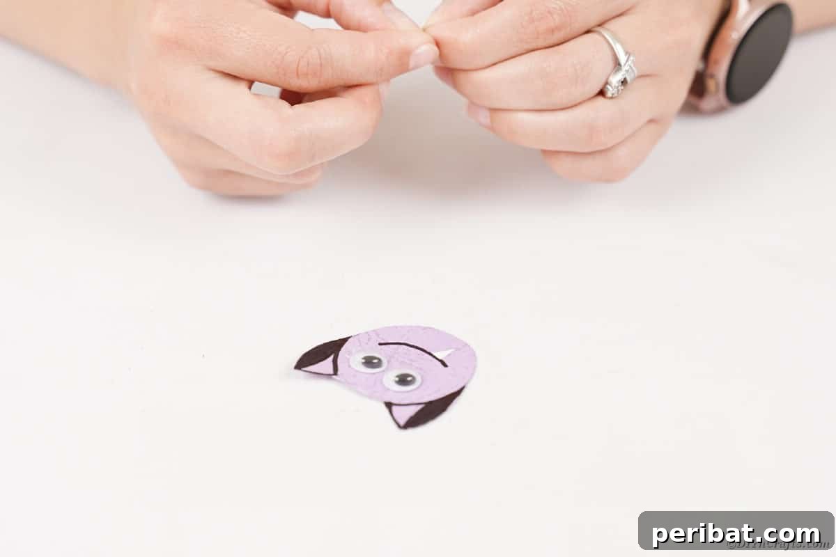 Spooky Paper Strip Creations: Bats, Pumpkins & Spiders 27 Small white paper triangles are being glued below the drawn smile on a purple bat face, forming fangs.