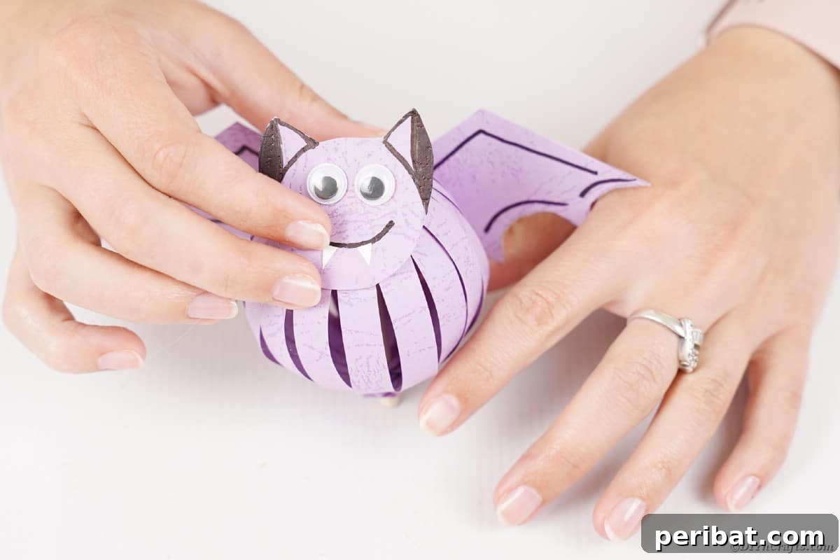 Spooky Paper Strip Creations: Bats, Pumpkins & Spiders 28 A woman holding a finished purple paper bat, showcasing its cute design with googly eyes and fangs.