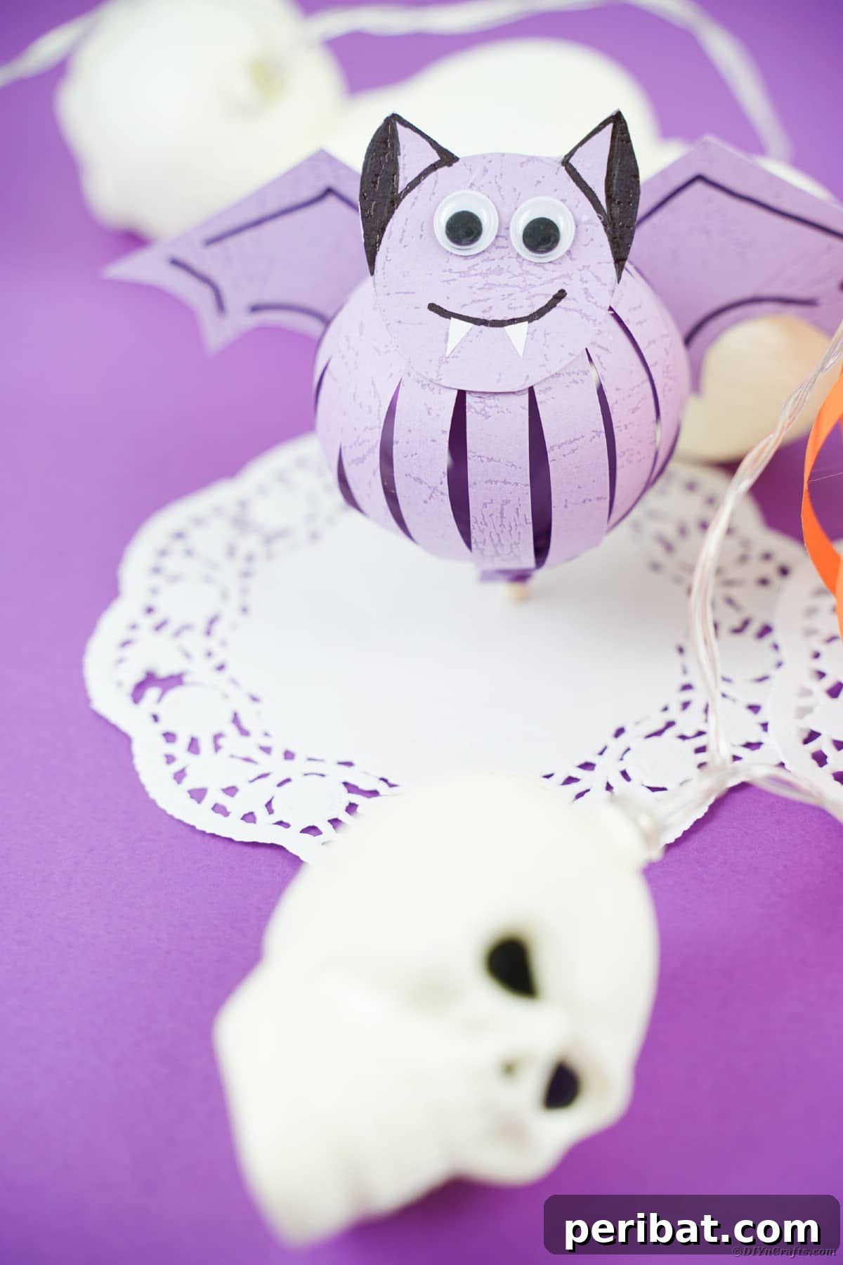 Spooky Paper Strip Creations: Bats, Pumpkins & Spiders 29 A finished purple paper bat with wide-open googly eyes and fangs, sitting on a white doily.