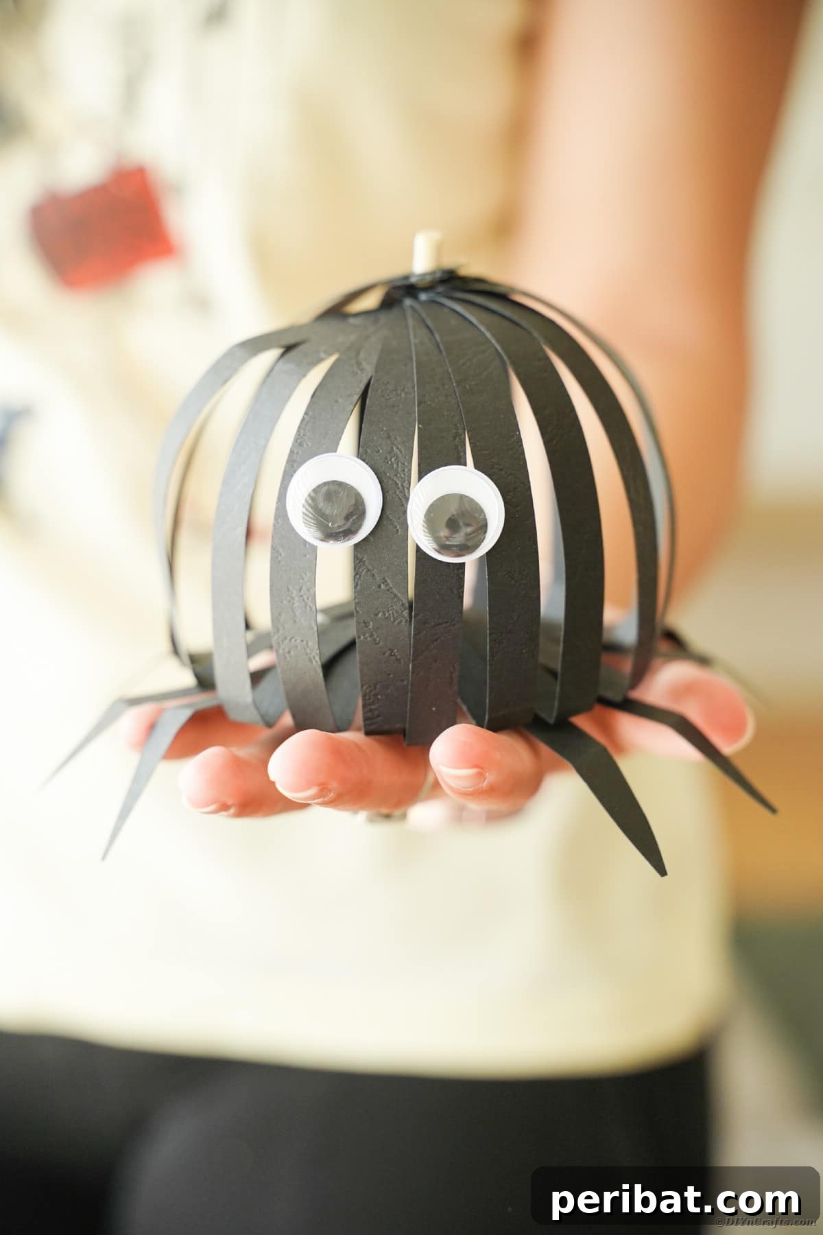 Spooky Paper Strip Creations: Bats, Pumpkins & Spiders 36 A woman proudly holding a finished black paper strip spider with googly eyes and articulated legs.