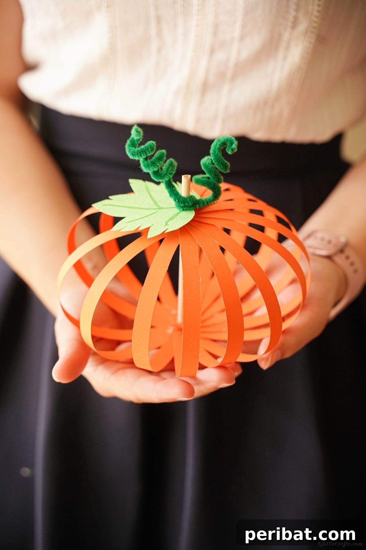 Spooky Paper Strip Creations: Bats, Pumpkins & Spiders 37 A woman holds a beautifully crafted orange paper strip pumpkin, its green stem and tendrils visible.