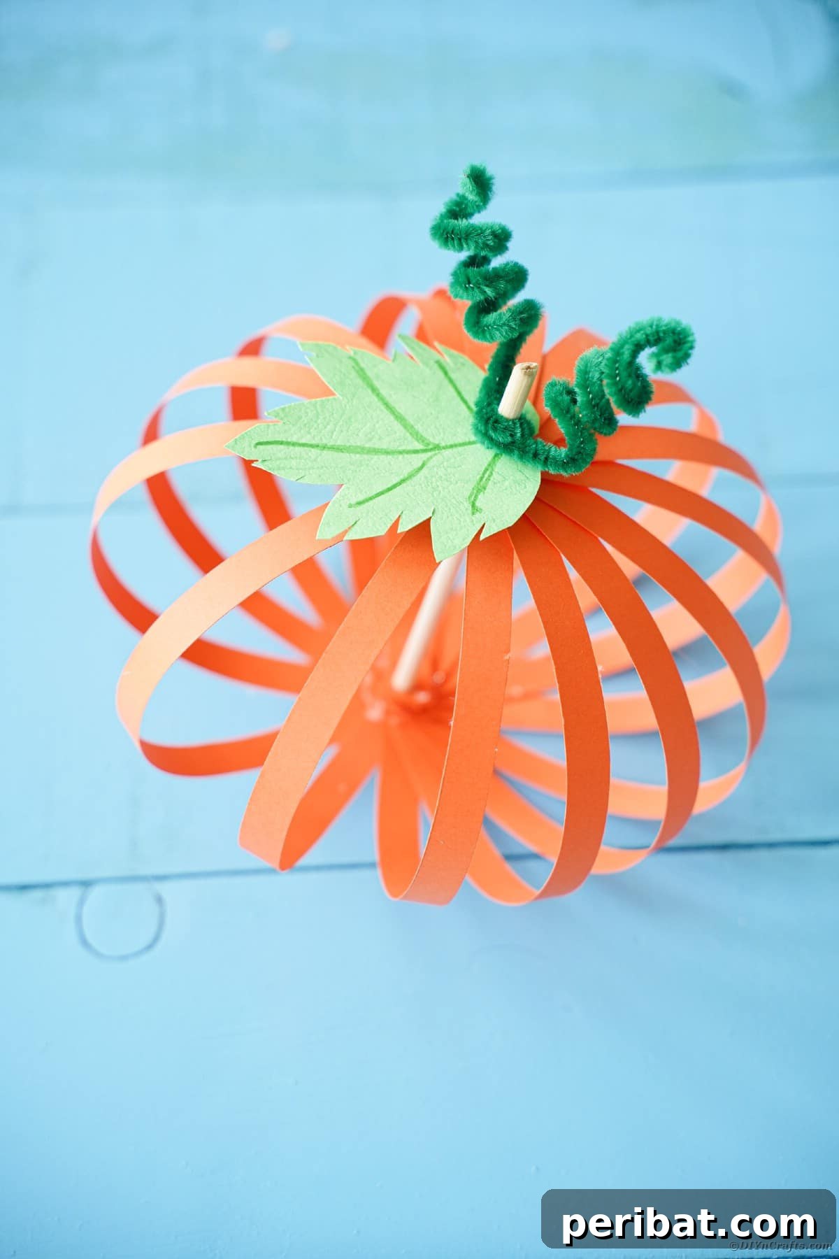 Spooky Paper Strip Creations: Bats, Pumpkins & Spiders 38 A paper strip pumpkin with a green stem sits on rustic blue wooden boards, ready for a fall display.