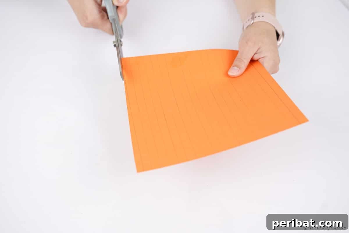 Spooky Paper Strip Creations: Bats, Pumpkins & Spiders 10 Scissors cutting multiple orange paper strips from a sheet, ready for crafting.