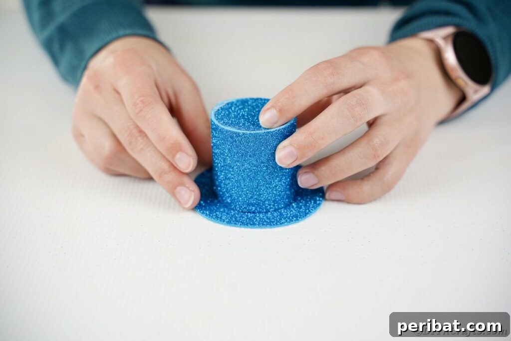 DIY Painted Tin Can Snowman Video Tutorial 18 A person gluing the hat brim onto the constructed hat body, completing the snowman's top hat.
