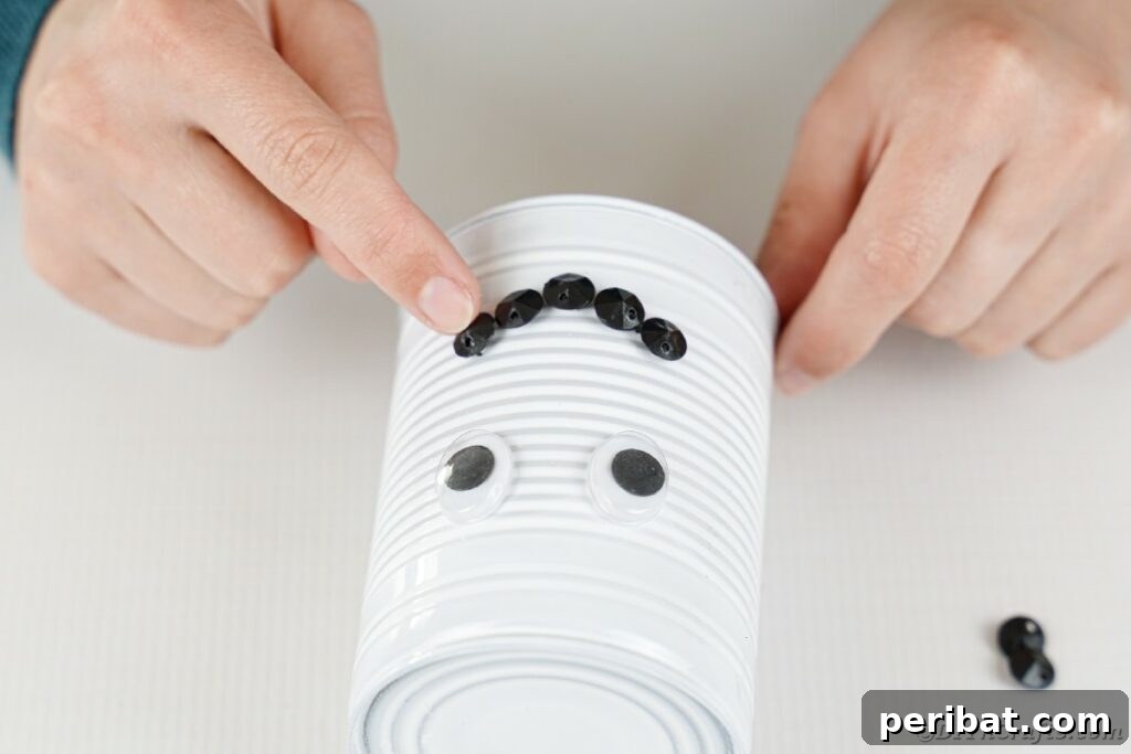 DIY Painted Tin Can Snowman Video Tutorial 20 Arranging and gluing black beads to form a smile on the snowman's tin can head.